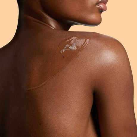 alt="Viscous serum drips down a glistening bare back, highlighting hydrated umber skin."