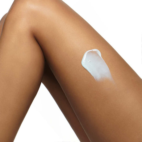 alt="Smooth sun-kissed legs with white body cream applied mid-thigh, against a pure white backdrop, highlighting product and skin fusion"