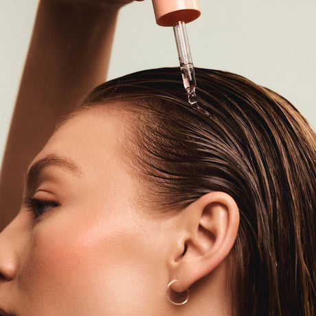 alt="Woman with black hair receiving a liquid droplet from a pink applicator, targeting her scalp for hydration"