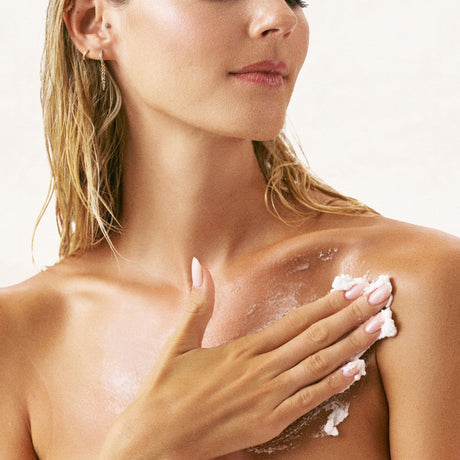 alt="Woman's hands holding white scrub applied to upper body against slate grey marble background"